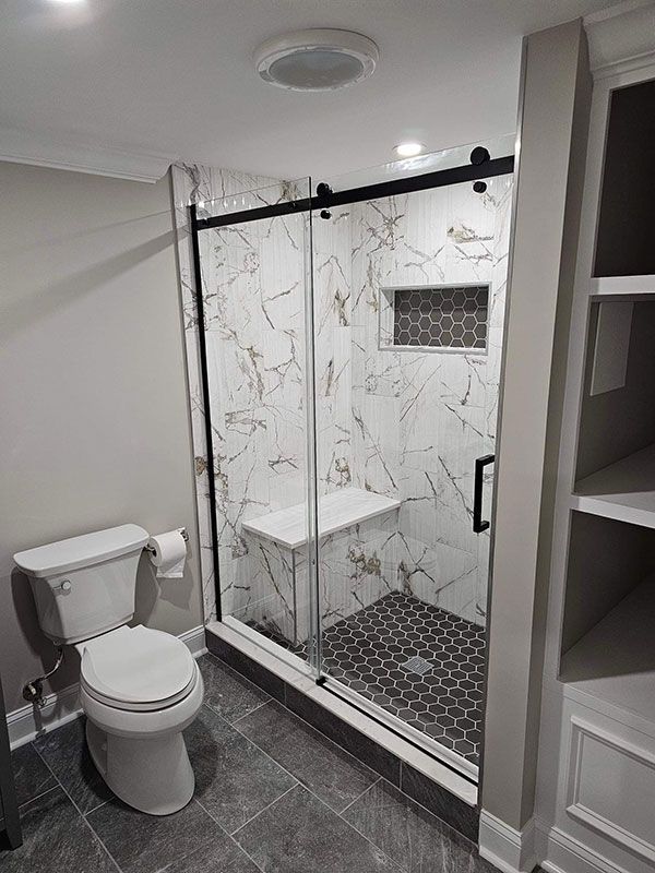 Bathroom with marble shower, built-in seat, black frame, gray tile floor, toilet, and shelving.
