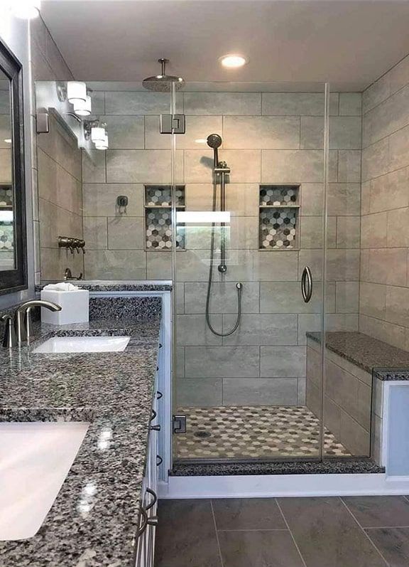 Modern bathroom with gray tiled walls, glass shower, granite countertop, and built-in bench.