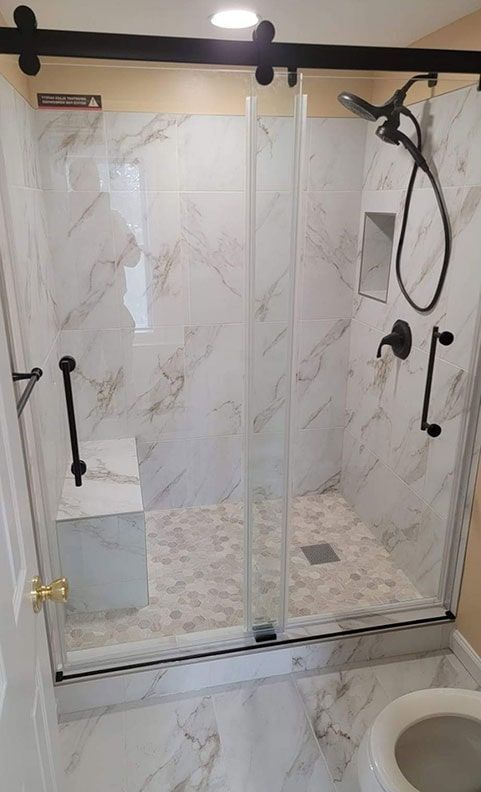 Bathroom with marble tile, sliding glass shower doors, and black fixtures.