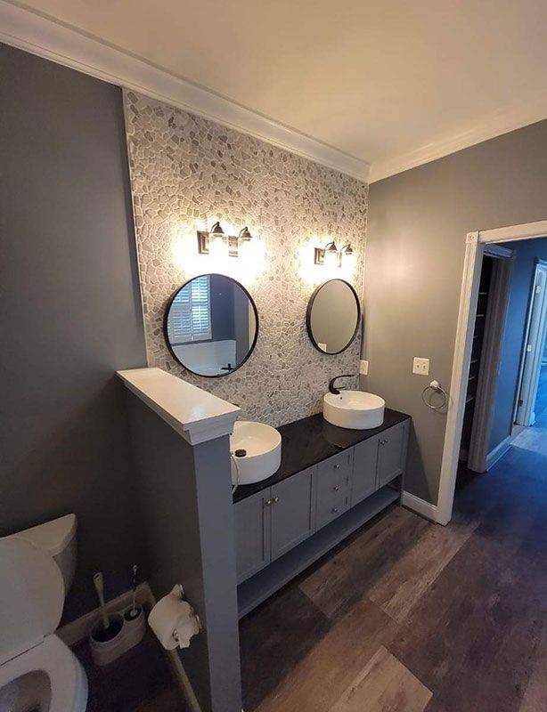 Bathroom with gray walls, two round mirrors, floating vanity, and vessel sinks.