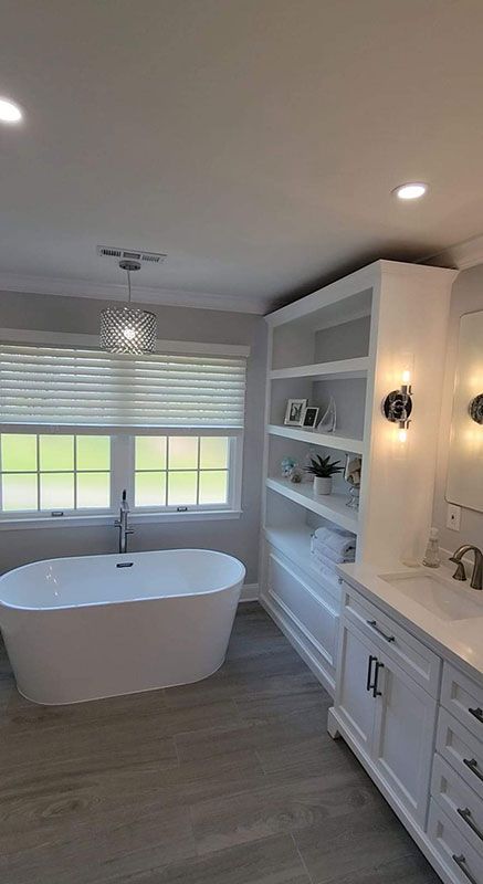 Modern white bathroom with freestanding tub, built-in shelving, and white vanity.