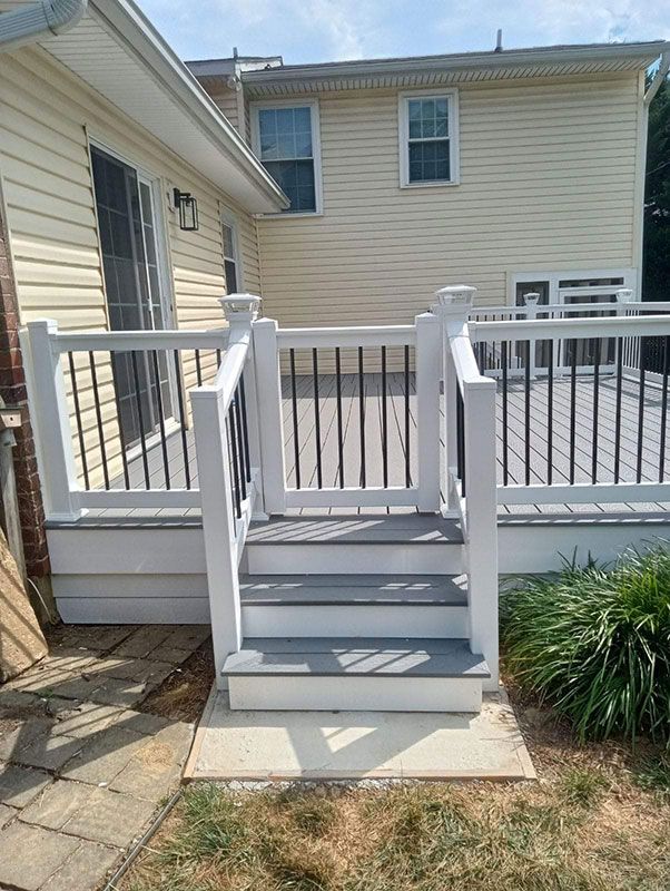 Composite deck with white railing, black balusters, and steps leading to a yard, beige siding background.