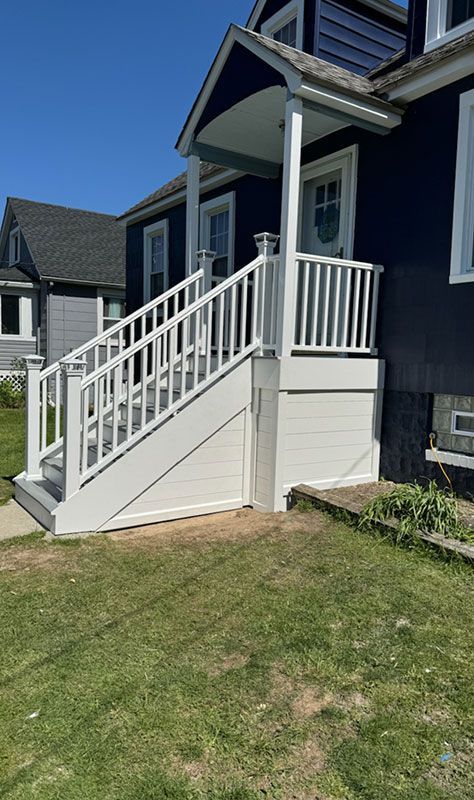 White porch with stairs leading up to a blue house. Green lawn and blue sky.