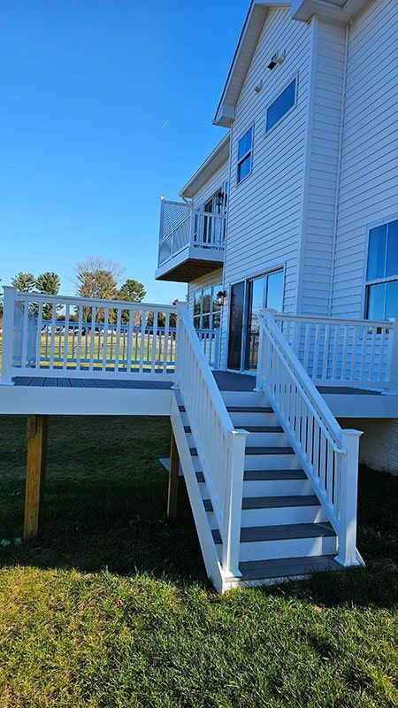 White house with outdoor deck and stairs, blue sky.