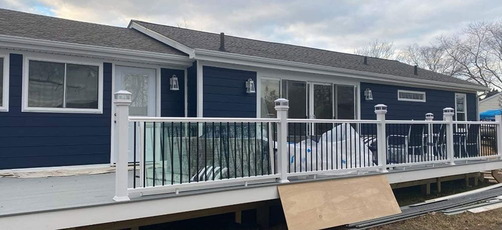 A dark blue house with a white deck and railing.  A sliding glass door and windows are visible. The sky is overcast.
