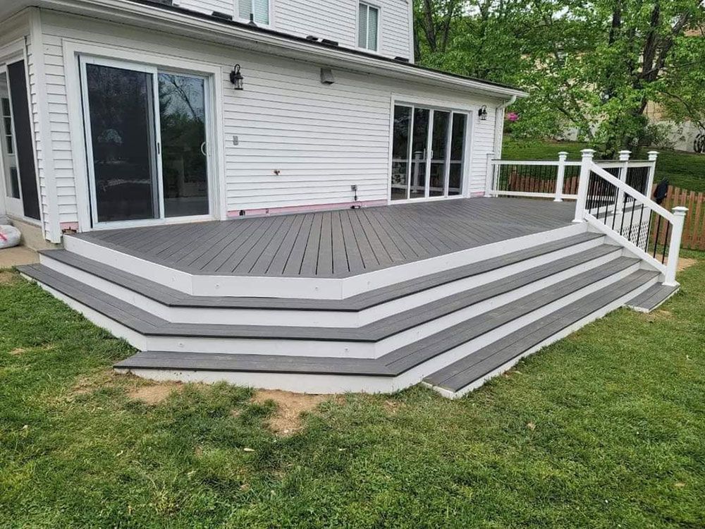 Gray deck with steps attached to a white house with sliding glass doors. White railing on the right.