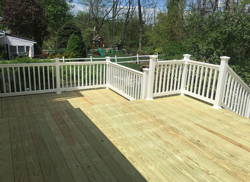 Wooden deck with white railing in a backyard setting; sunny day.