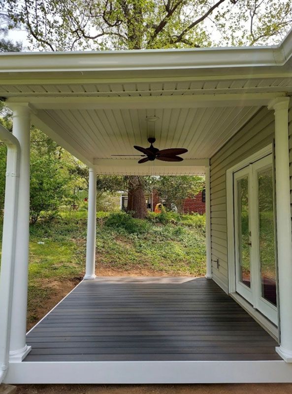 Covered porch with dark gray deck, white columns, ceiling fan, and French doors leading inside.