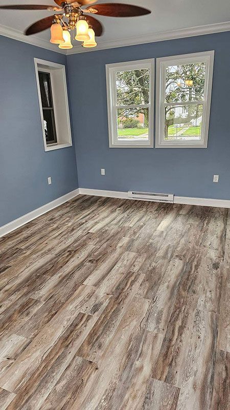 Empty room with blue walls, wood-look flooring, and three windows.
