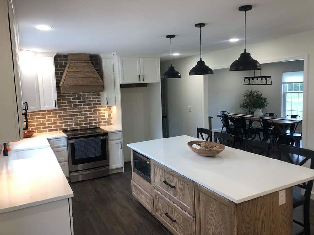 Kitchen with white countertops, brick backsplash, wooden island and range hood, black pendant lights.