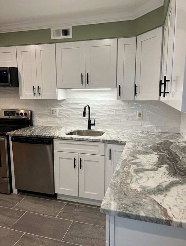 White kitchen cabinets with granite countertops, stainless steel appliances, and a black faucet.