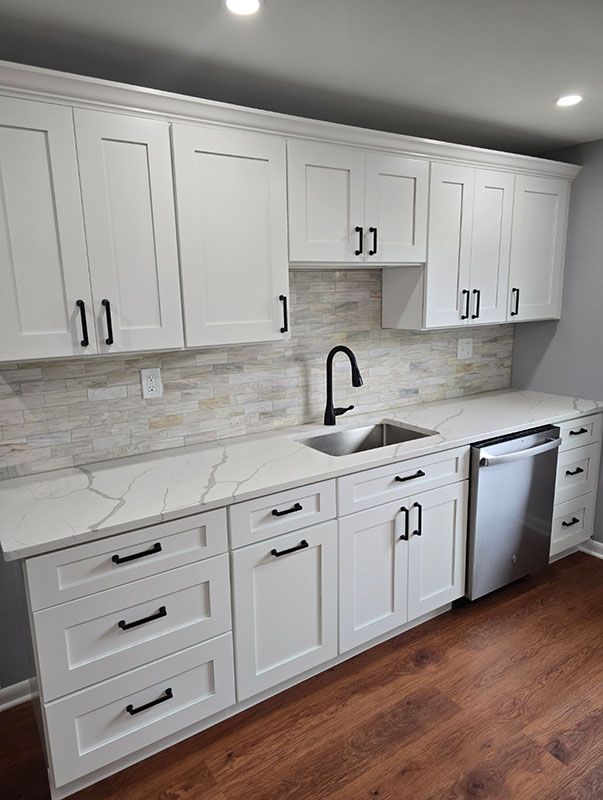 White kitchen cabinets with black handles, white countertops, and stainless steel appliances.