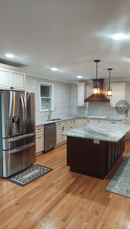 Newly renovated kitchen with wood floors, stainless steel appliances, and a dark island with granite countertops.