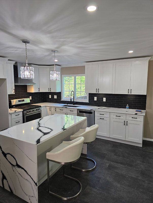 Modern white kitchen with black backsplash, island with quartz countertop, and silver appliances.