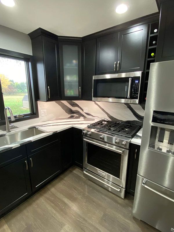 Black kitchen cabinets with a stainless steel range, microwave, and refrigerator, next to a sink.