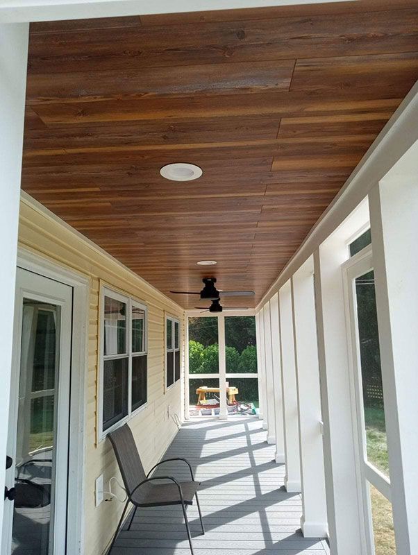 Enclosed porch with wood ceiling and fan. Chair on composite floor, windows, and white columns.
