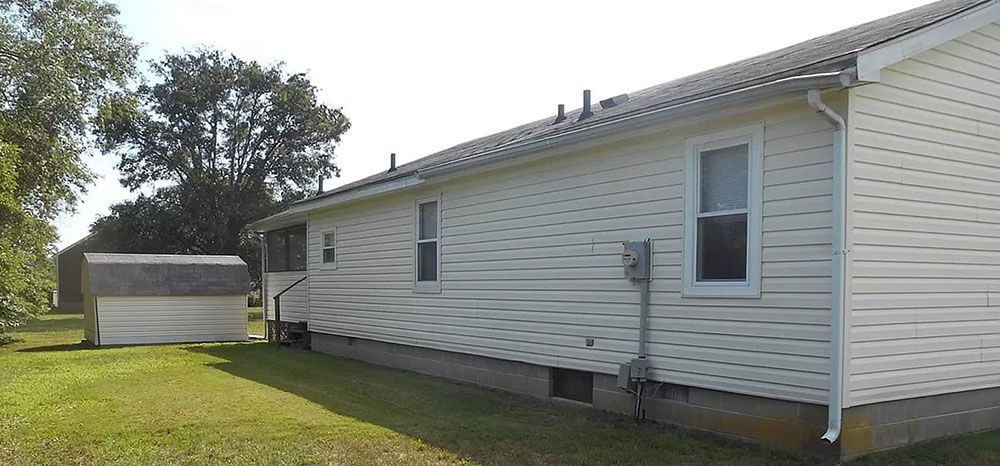 Side view of a white house with a shed in the yard on a sunny day.