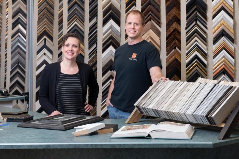 A man and a woman are standing in front of a table with frames on it.