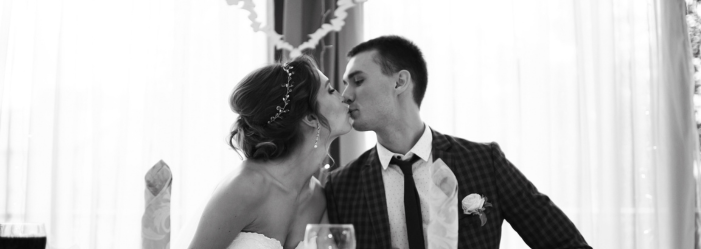 A black and white photo of a bride and groom kissing at a wedding reception.