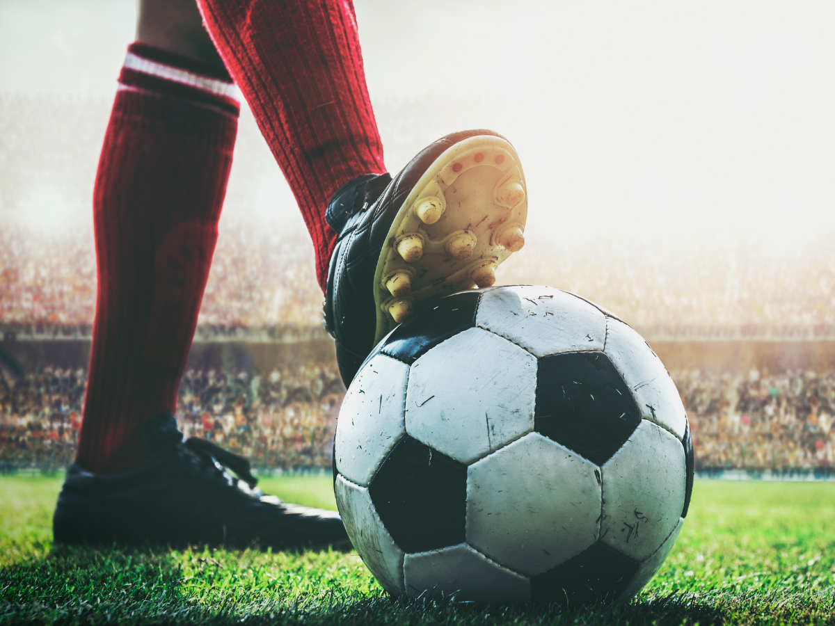 Soccer player’s cleat on a black-and-white ball on a grassy field with stadium lights in the background