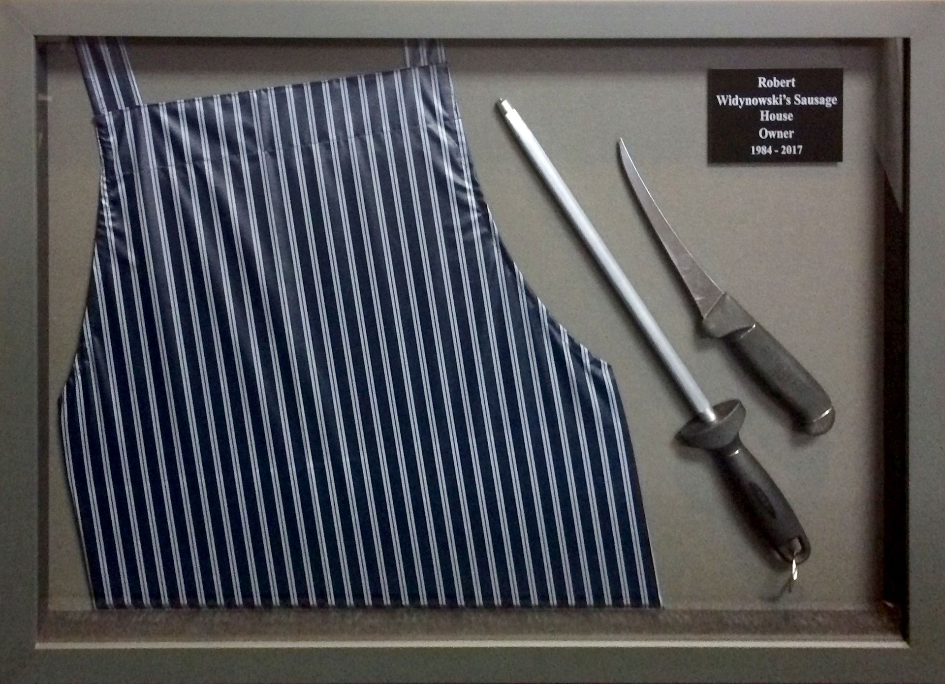 A framed picture of a blue apron and knives