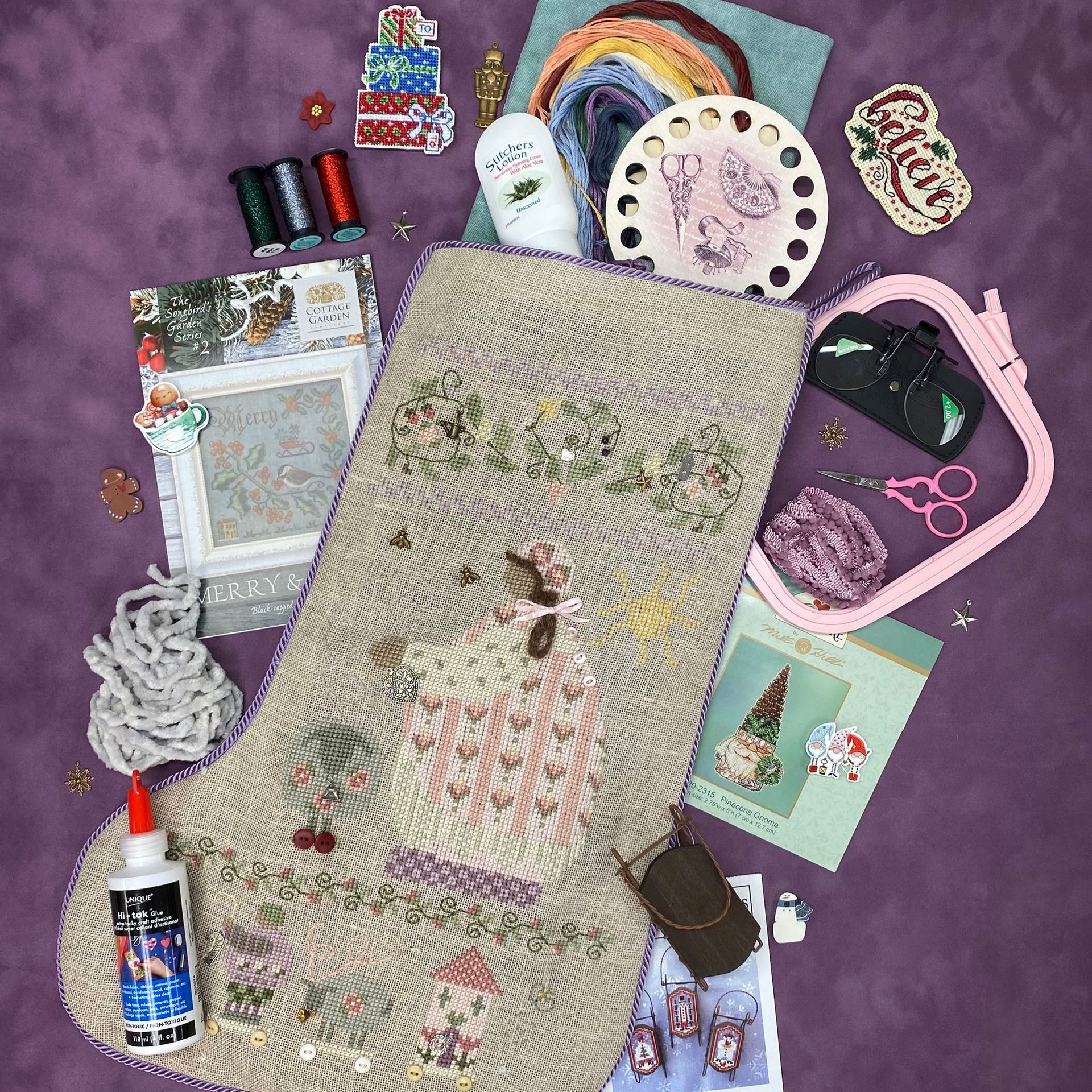 A christmas stocking is surrounded by sewing supplies on a purple surface.