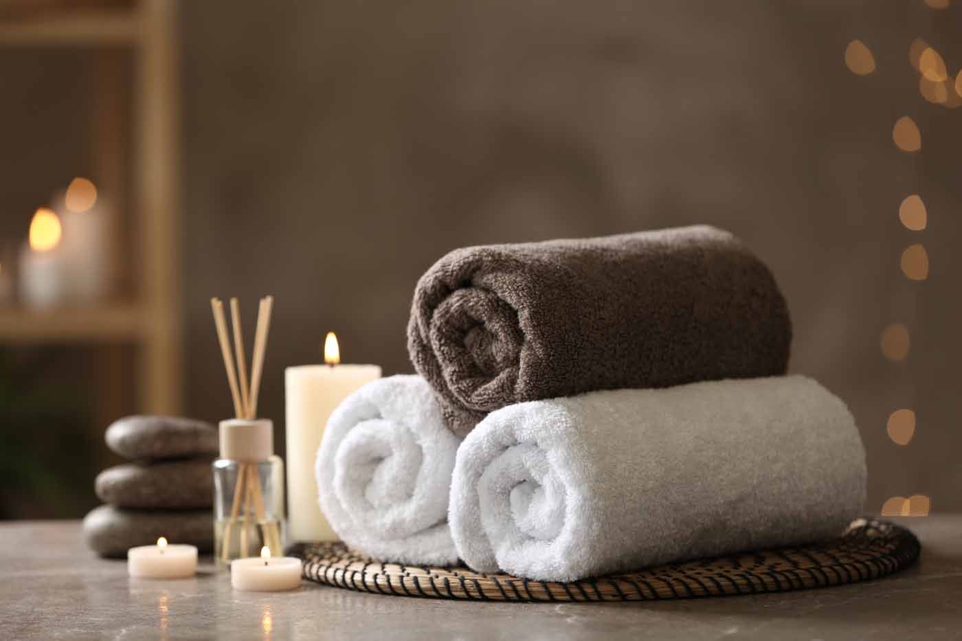 A stack of towels , candles , and rocks on a table in a spa.