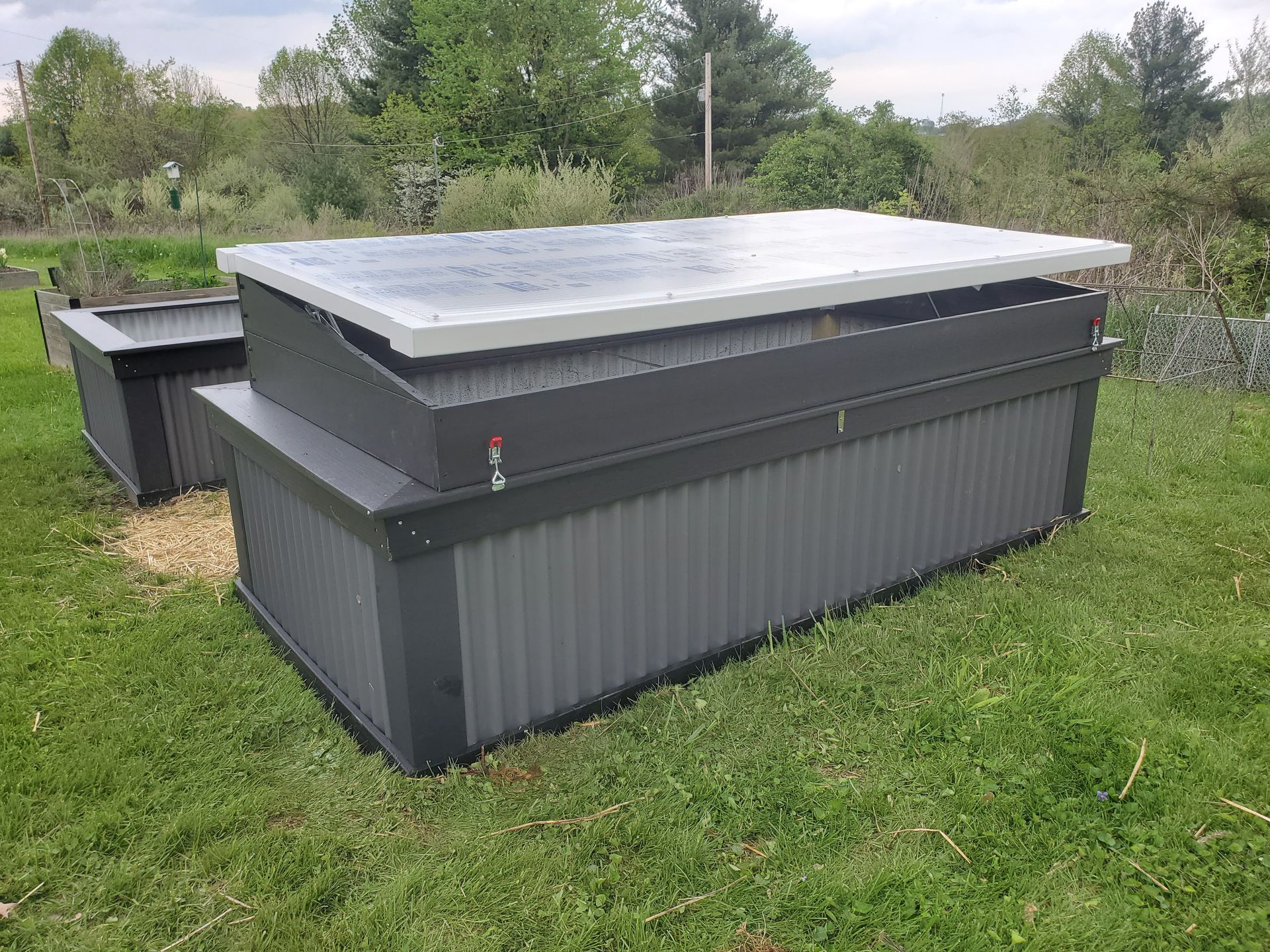 Two dark gray compost bins on a grassy lawn with trees in the background.