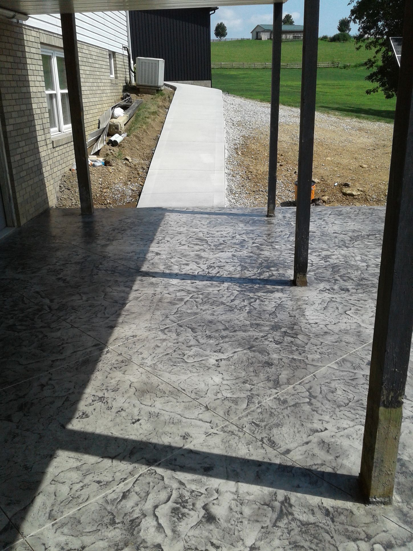 Stamped concrete patio with support posts, leading to a walkway beside a building.