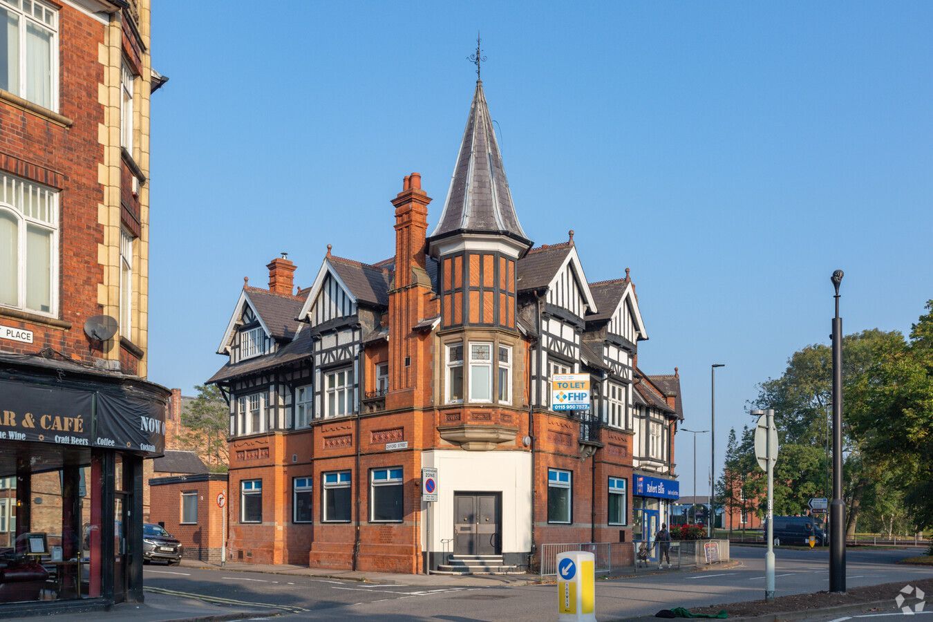 A large brick building with a tower on top of it is on the corner of a street.