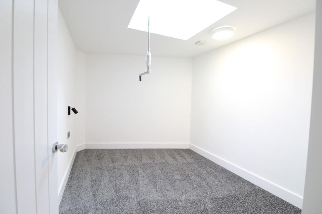 An empty room with a skylight and a gray carpet.