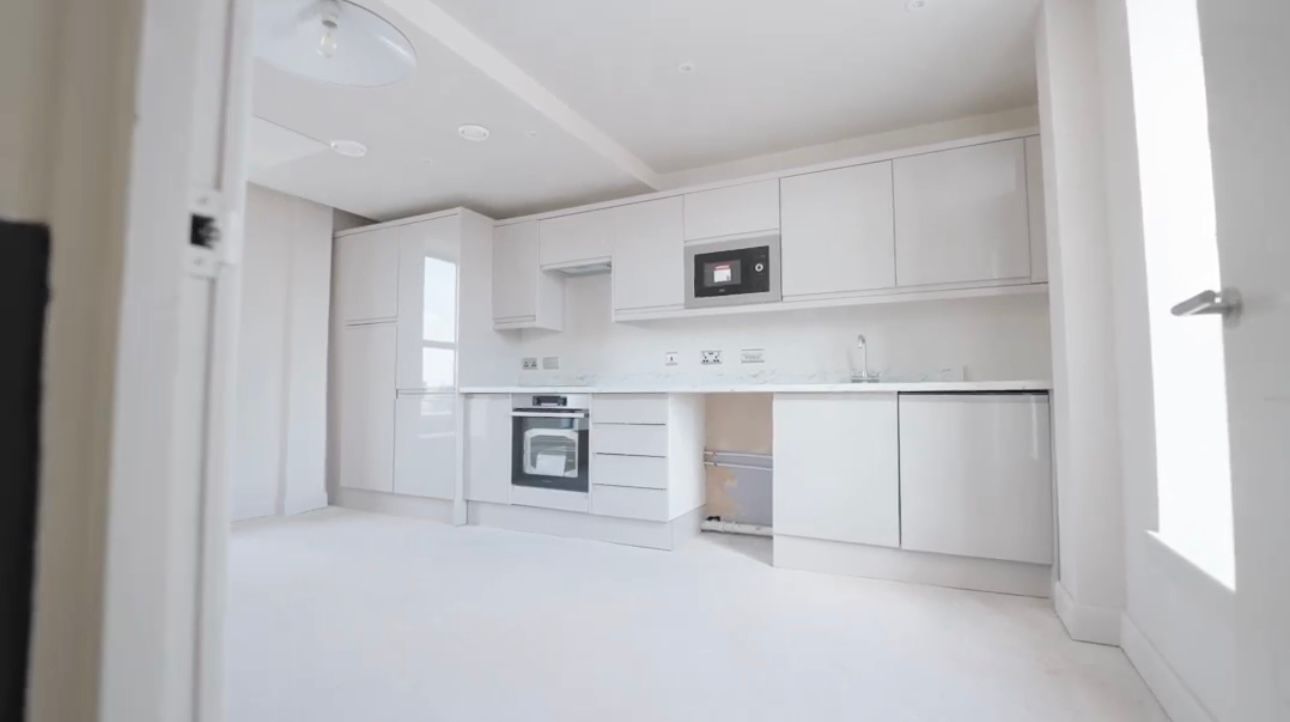 An empty kitchen with white cabinets , appliances , and a window.