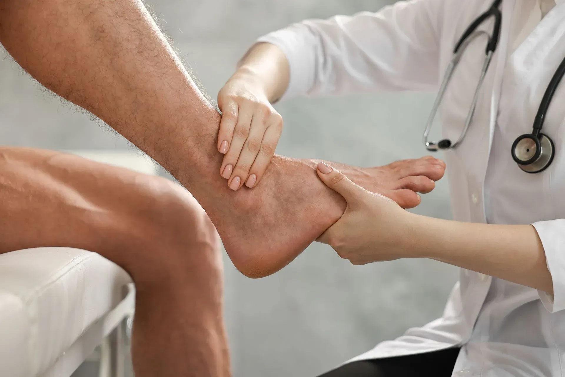 A healthcare professional in a white coat with a stethoscope examines a patient's ankle.
