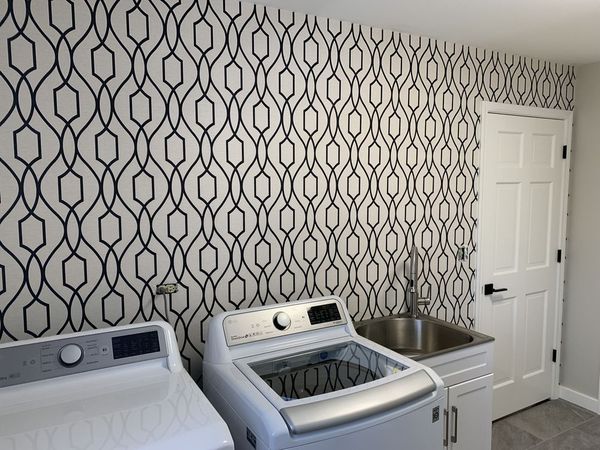 Laundry room with black and white geometric wallpaper, white appliances, and a utility sink.