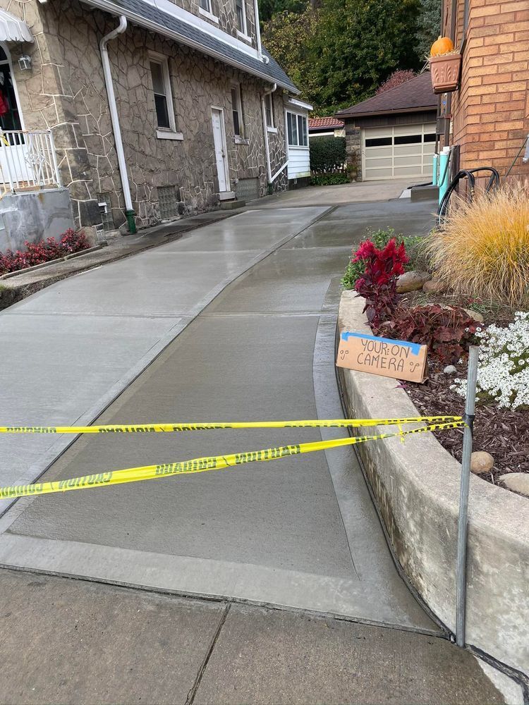 Freshly poured concrete driveway blocked with caution tape, beside a house with a garden.