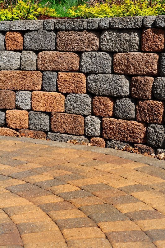 Stone retaining wall with a paved brick patio, featuring brown and gray bricks.