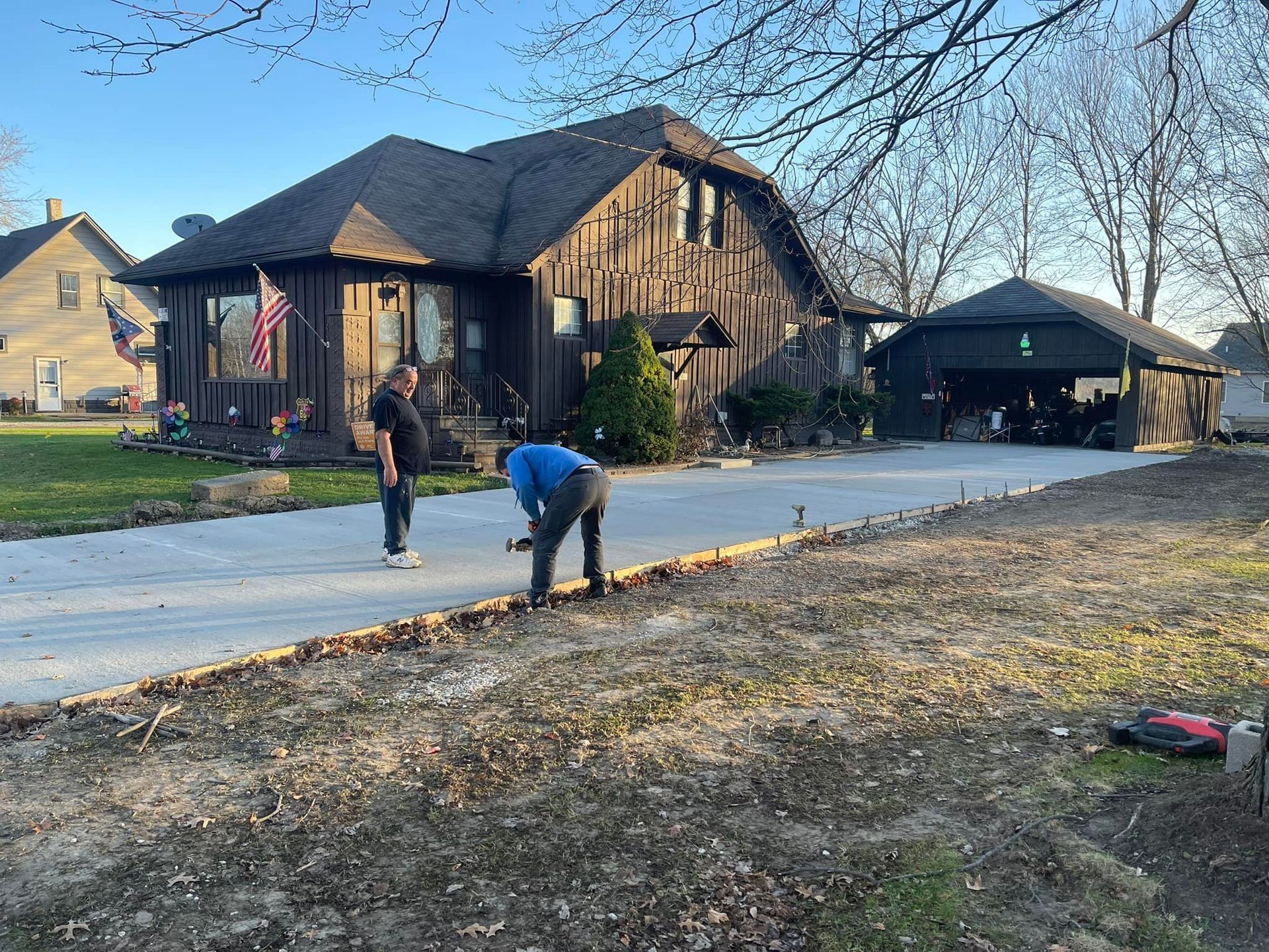 Two people working on a new concrete driveway in front of a brown house and garage.