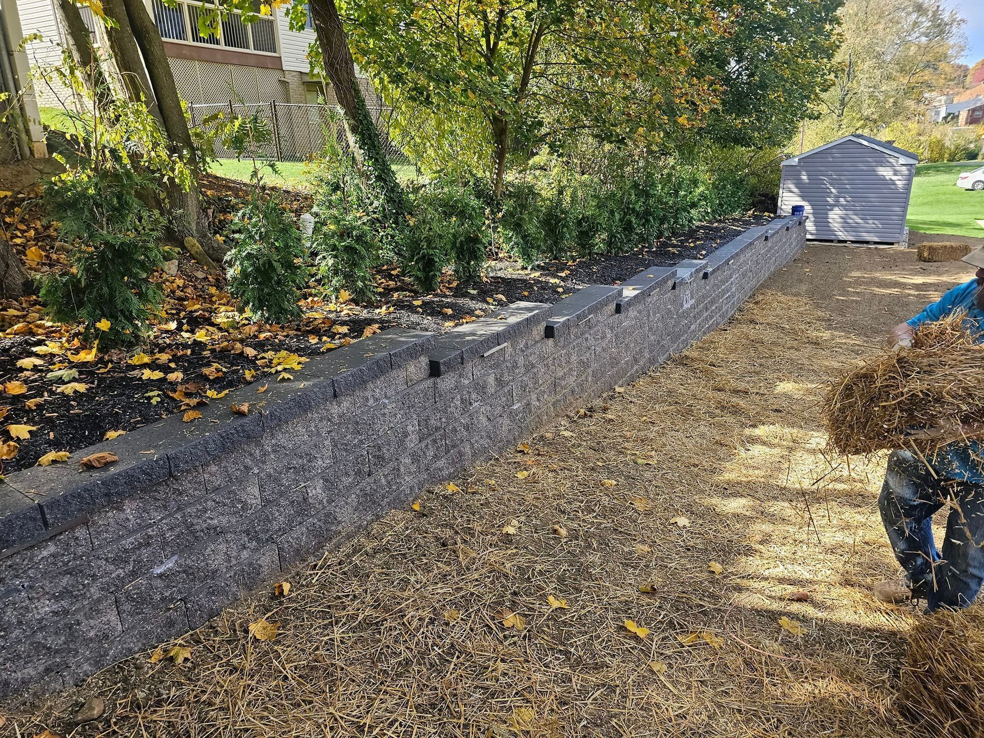 A person spreading mulch alongside a retaining wall and garden bed.