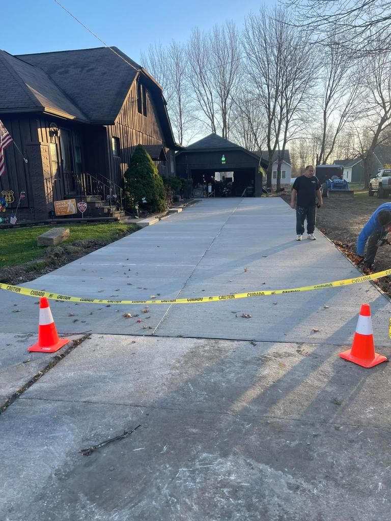 New concrete driveway with caution tape and cones in front of a house, workers nearby.