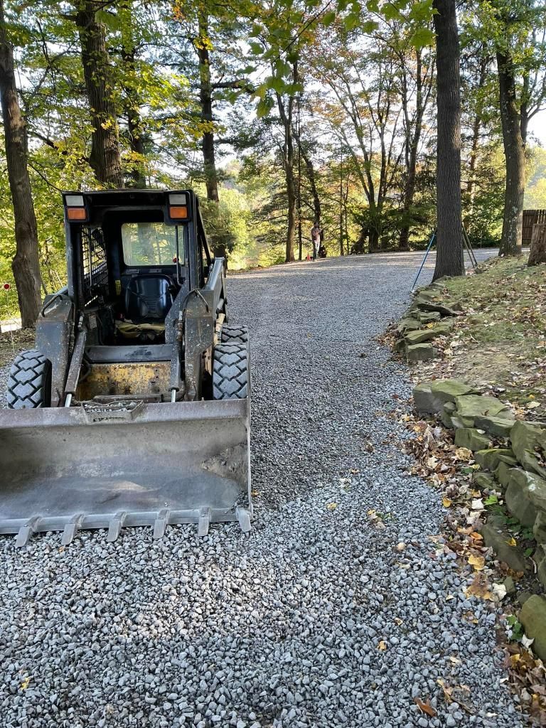 Skid steer on a gravel driveway, trees in background.