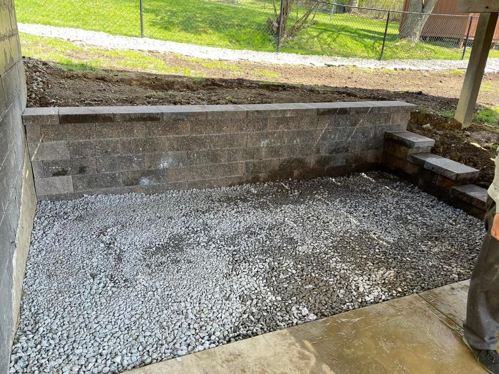 Small gravel patio area with retaining wall and steps; next to a concrete surface.