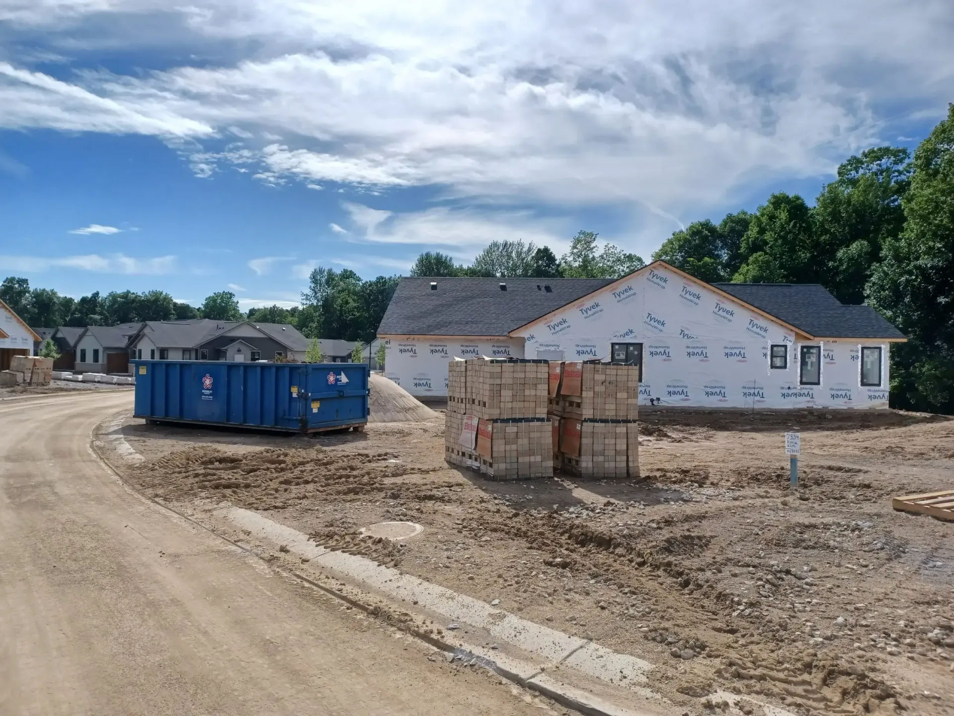 Construction site with new homes, a blue dumpster, and materials under a cloudy sky.