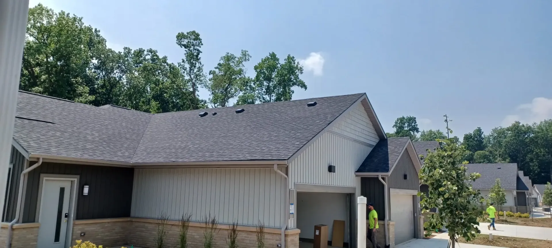 New houses under construction with dark gray roofs, white siding, and green trees.