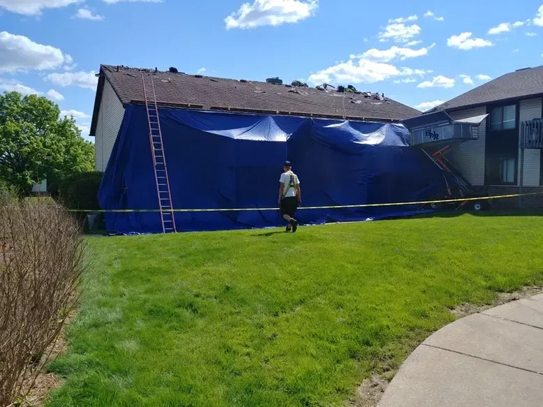 A building under a blue tarp for roof repair with a person walking on grass.