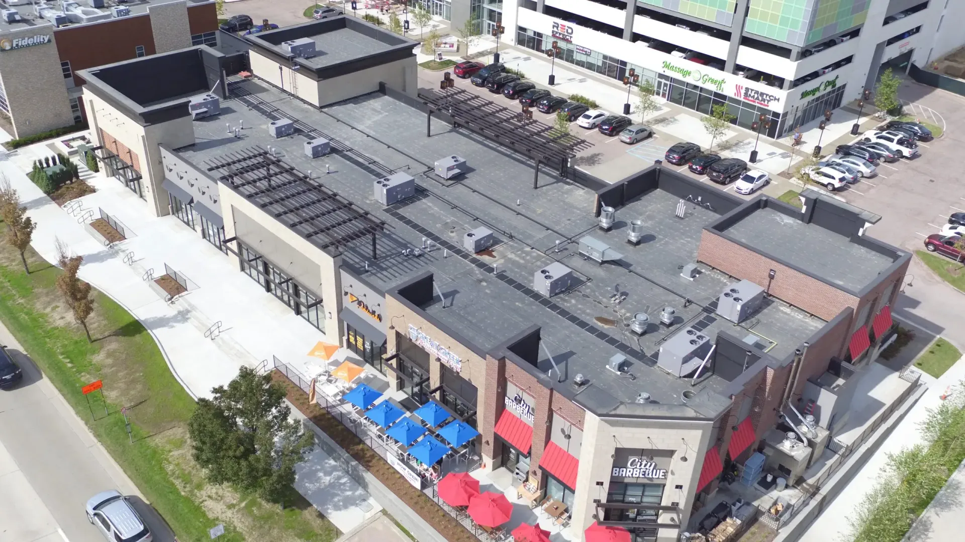 Aerial view of a retail building with a flat roof, multiple storefronts, and outdoor seating with blue umbrellas.