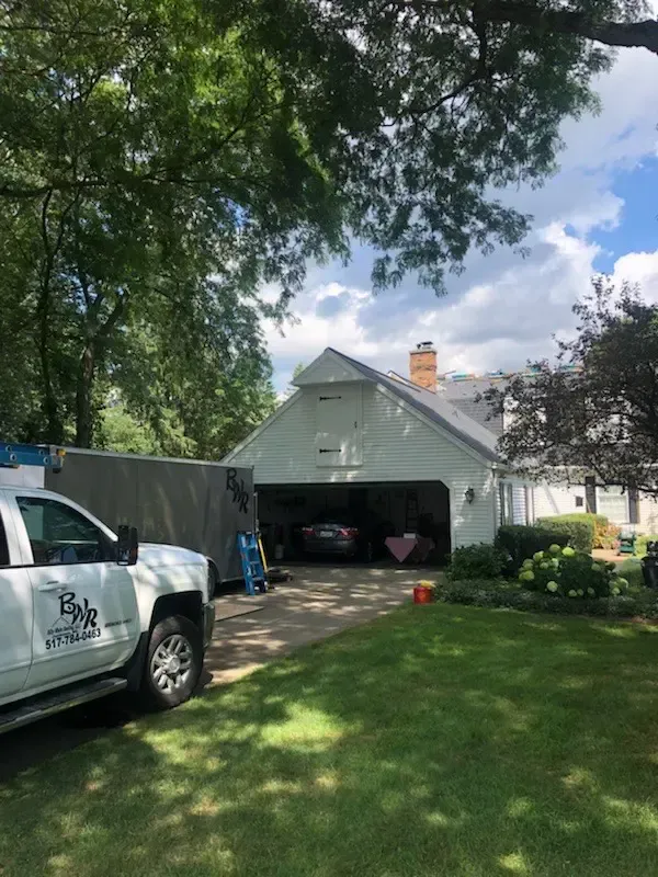 White garage with open door, a truck, and a house under a bright sky.