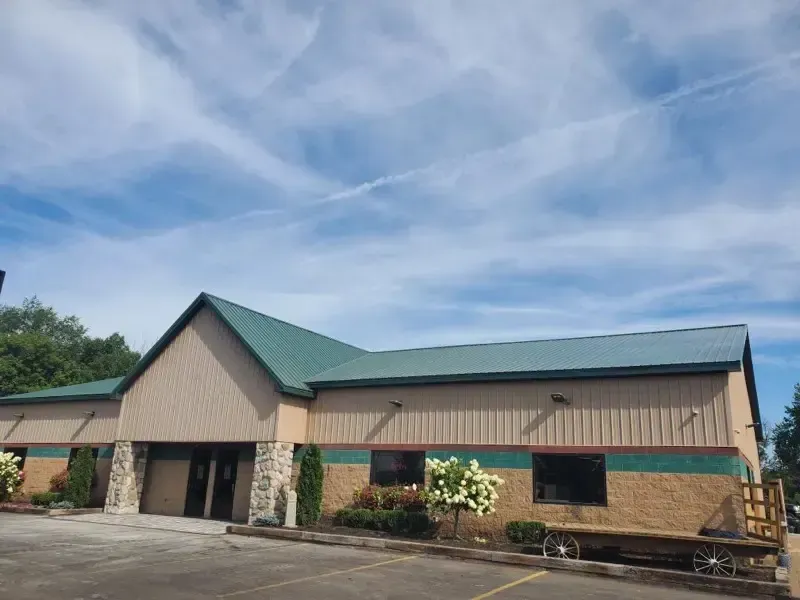 Tan commercial building with green roof and trim under a blue sky.
