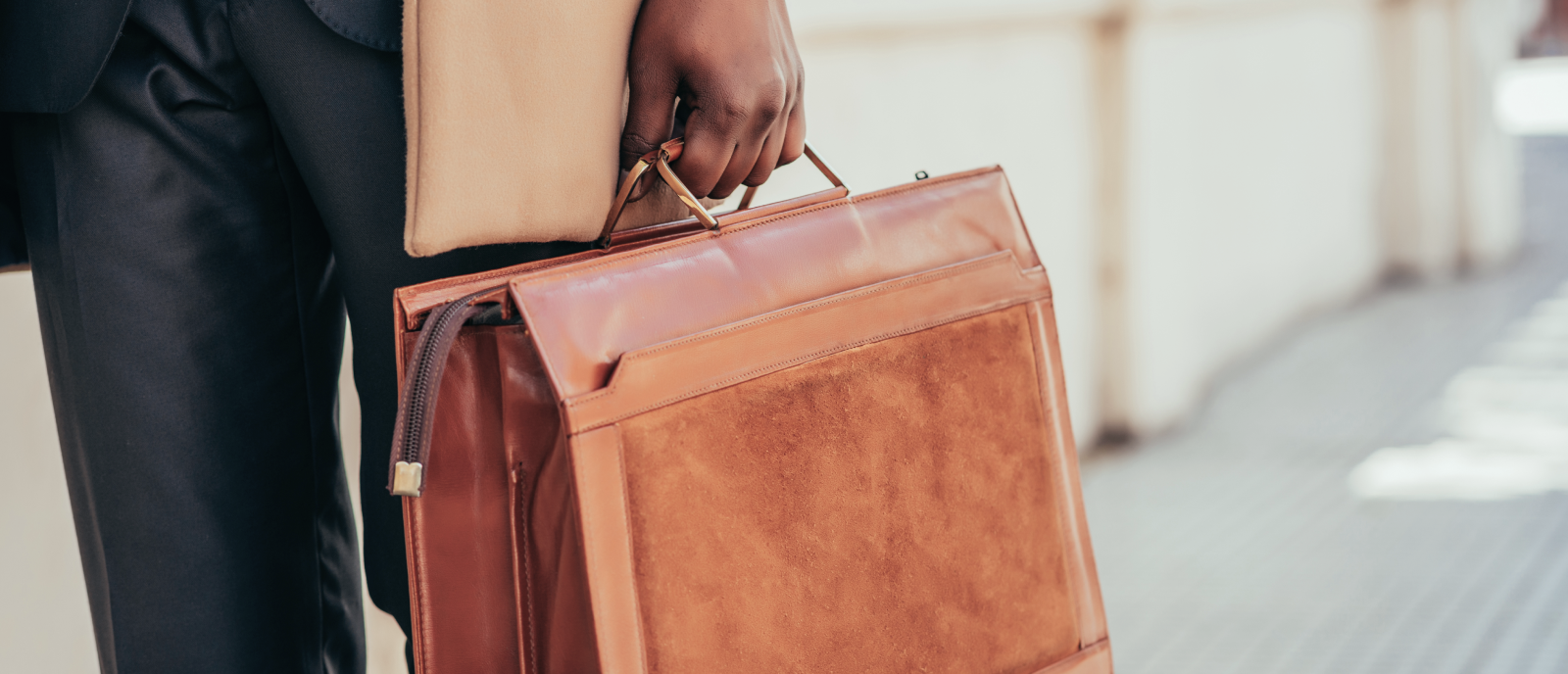 A man in a suit is holding a brown leather briefcase.
