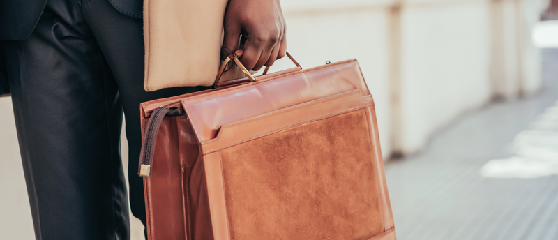 A man in a suit is holding a brown leather briefcase.