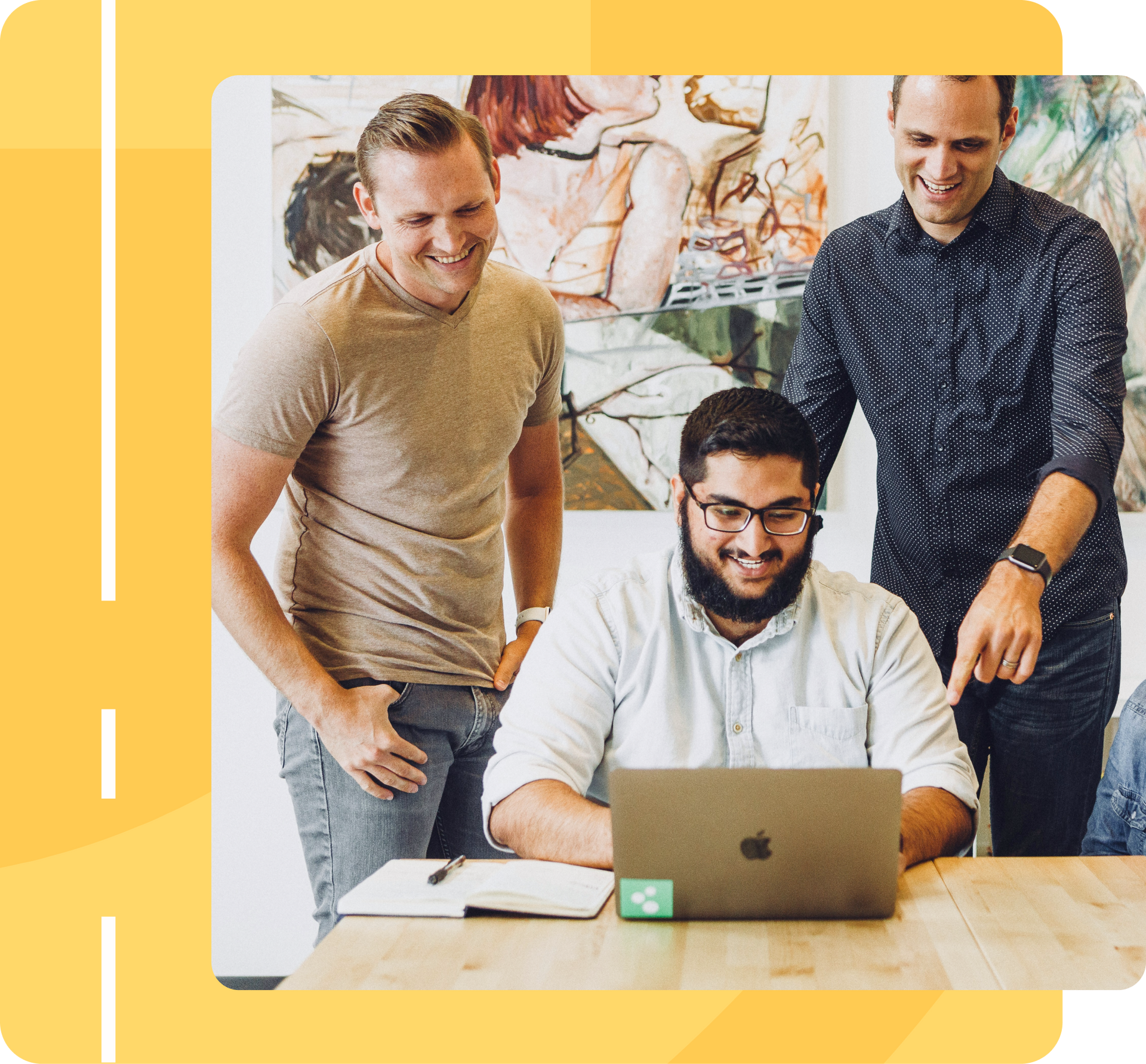 Three men are standing around a table looking at a laptop.